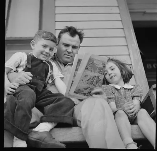 Black and white photo of a father reading to two children on porch steps