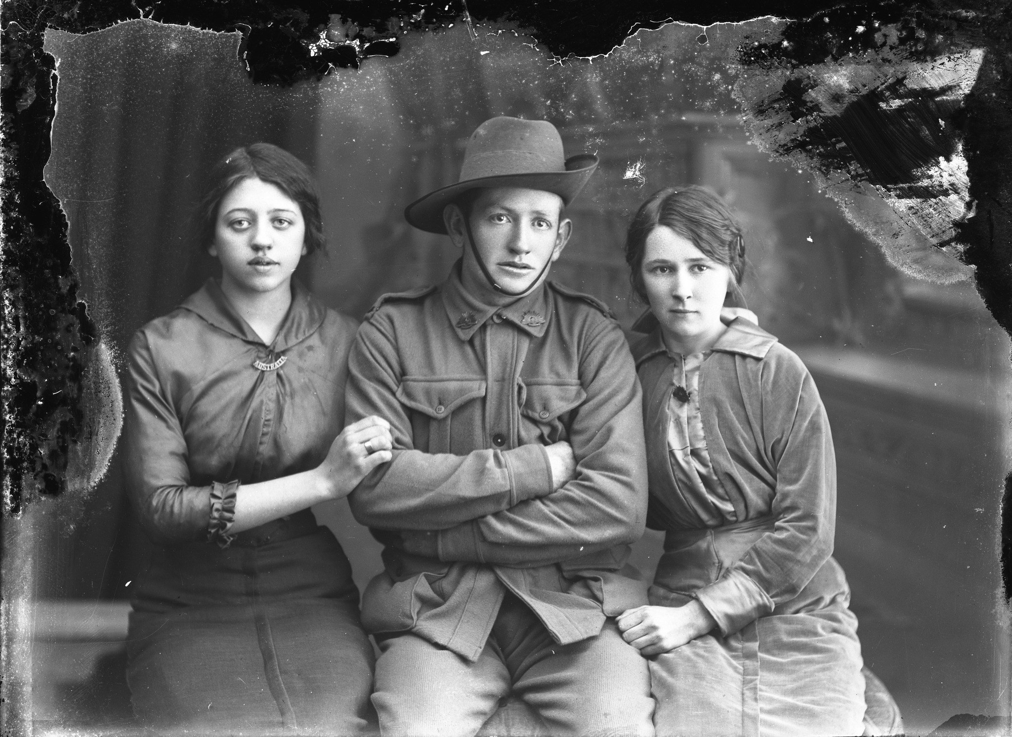 Damaged WW1-era black and white photograph of a soldier in uniform seated with two young daughters, heavy creases and stains across the surface